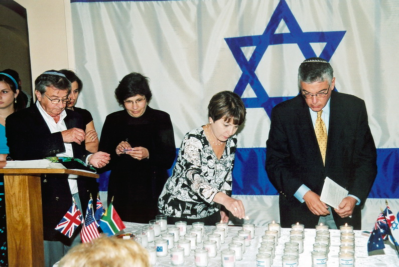 Kupiškio žydų palikuonys uždega žvakutes prie savo sušaudytų protėvių atminimo lentos Kupiškio viešojoje bibliotekoje. Pirmas iš kairės – Normanas Mejeris, dešinėje – Harvis Šerzeras. KUPIŠKIO ETNOGRAFIJOS MUZIEJAUS ARCHYVO nuotr.  